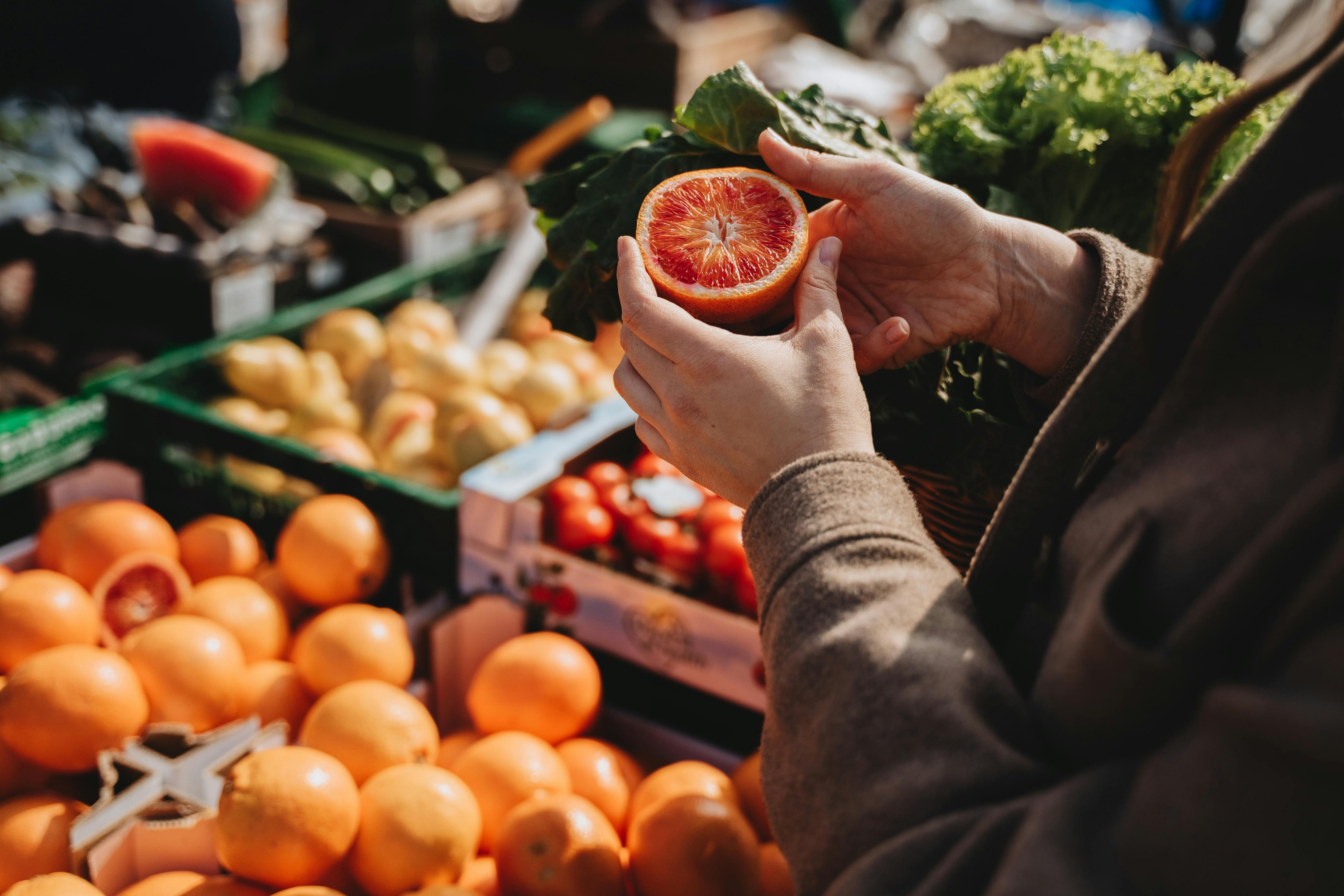 someone holding cut fruit while surrounded by fresh fruit stands