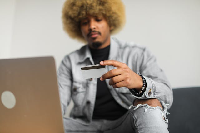 man holding up a credit card while typing on an open laptop
