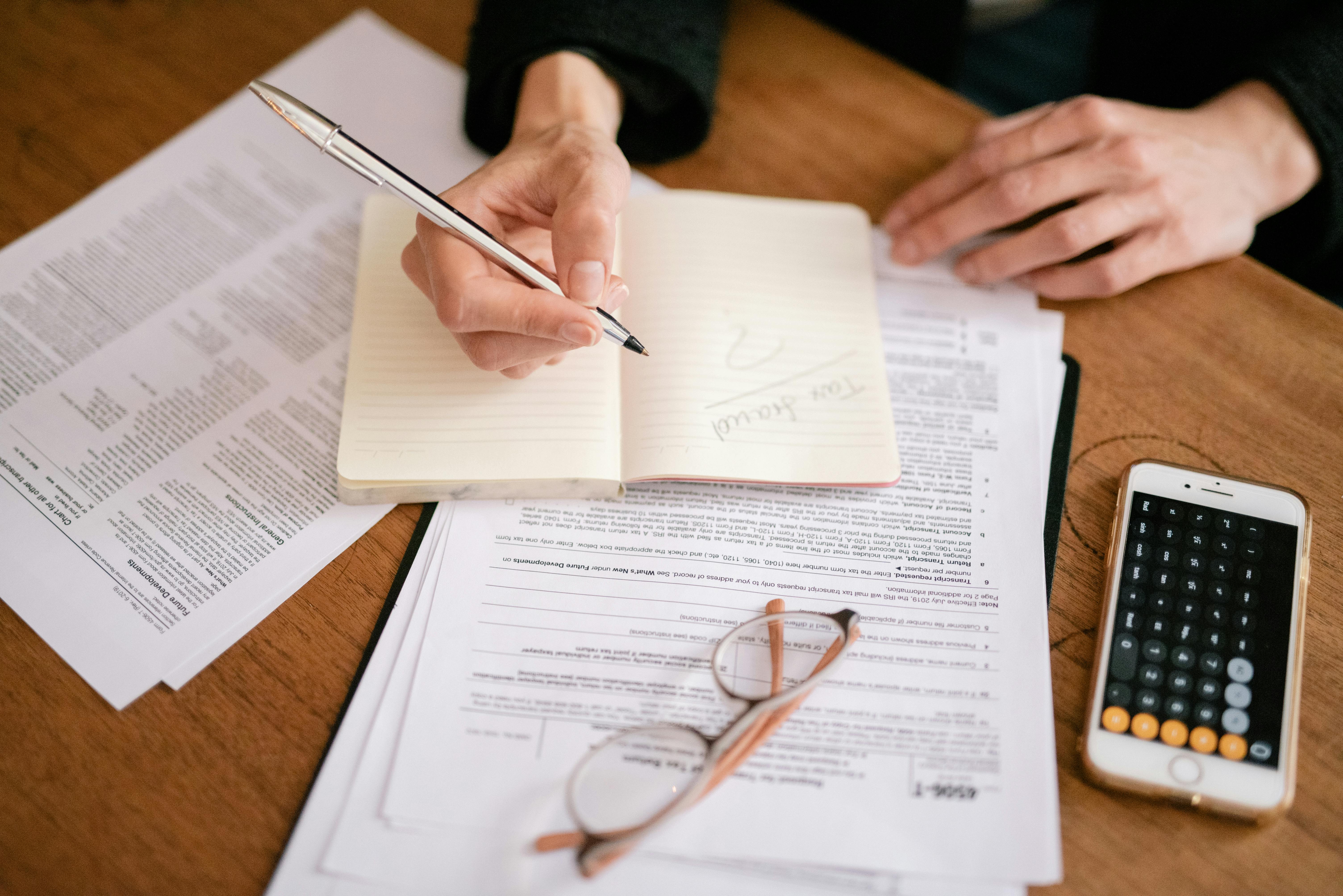 someone filling out tax forms while writing in a notebook and using a calculator