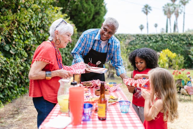 backyard barbecue with two older people and two children getting hot dogs