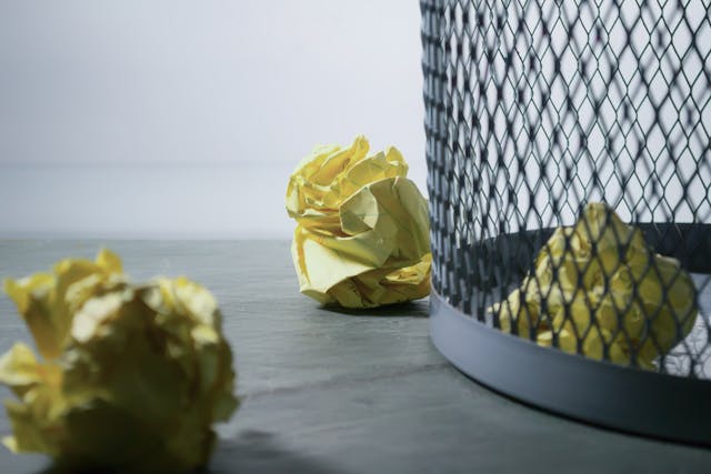 crumpled up yellow paper balls next to a wire trash can
