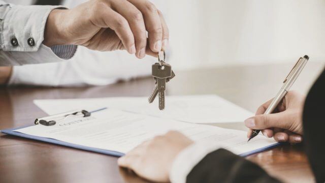 person dangling a key over someone else who is signing a document