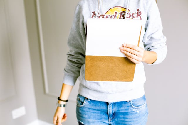 A person in a gray sweater and jeans holding a clipboard